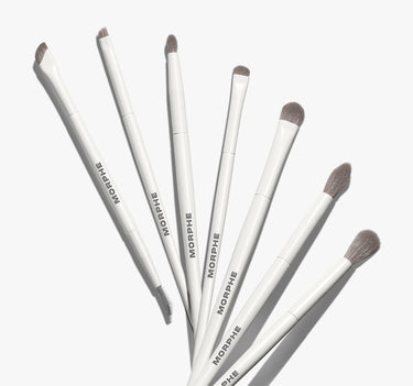 Morphe Eye Want It All 7 Piece Eye Brush Set — seven white MORPHE-labeled brushes with gray bristles fanned out, featuring varied tip shapes for eye looks.
