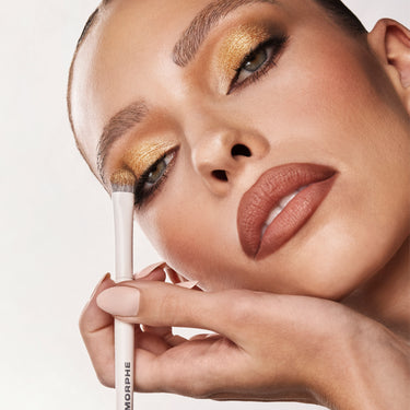 {Flickering Sands} Model wearing Chromaplus 12 Pan Eyeshadow Palette in golden and bronze tones with charcoal crease, holding a MORPHE brush.