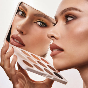 {Flickering Sands} Model holding open Chromaplus 12 Pan Eyeshadow Palette with warm gold and bronze eye look reflected in the palette mirror.