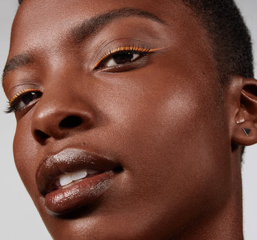 {Deep 34W} Close-up model shot of Lightform Extended Hydration Foundation on deep skin, showcasing a luminous, dewy finish with orange liner and glossy lip.