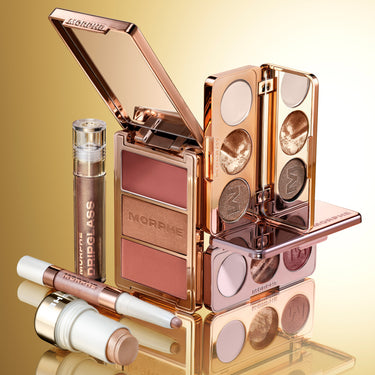 Stylized group shot of the Trophy Wife Collection featuring the Cheek Thrills Multi-Finish Face Trio compact with MORPHE engraved lid open beside an eyeshadow palette and Dripglass lip gloss.