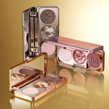 Stylized group shot of three open Dazzling Metallics Eyeshadow Trio compacts with MORPHE engraved on lids, showcasing all shades in silver and rose-gold packaging against a golden background.