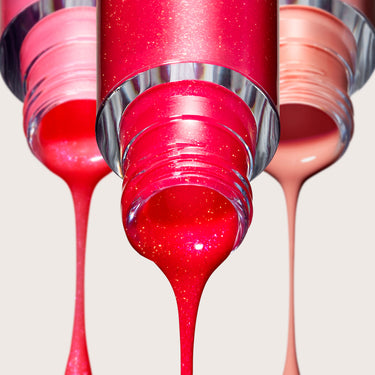 Three Dripglass Glazed High Shine Lip Gloss tubes dispensing drips of shimmery red, pink, and nude gloss formula. & Three Dripglass Glazed High Shine Lip Gloss tubes dispensing drips of shimmery red, pink, and nude gloss formula.