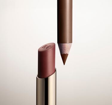 Lip Filter Signature Lip Bundle close-up of a mauve lip balm stick with embossed M logo beside a sharpened brown lip liner pencil.