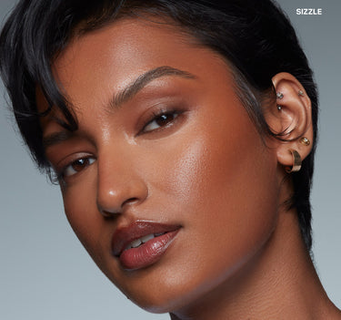 {Sizzle} Model wearing Sudden Heat Creamy Bronzer Stick in Sizzle with warm bronze glow on cheeks and luminous skin finish; text reads SIZZLE