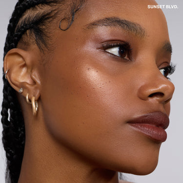 {Sunset Blvd.} Model wearing Dreamlight Gelee Highlighter Stick in Sunset Blvd. with a luminous, glowing highlight on cheekbones — "SUNSET BLVD." text overlay.